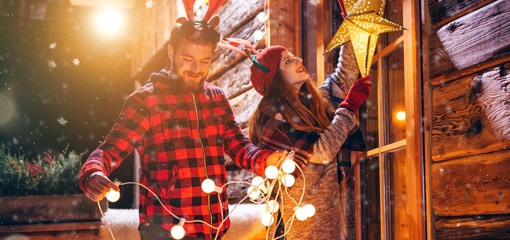 Man and woman decorating the outside of their house with Christmas decorations.