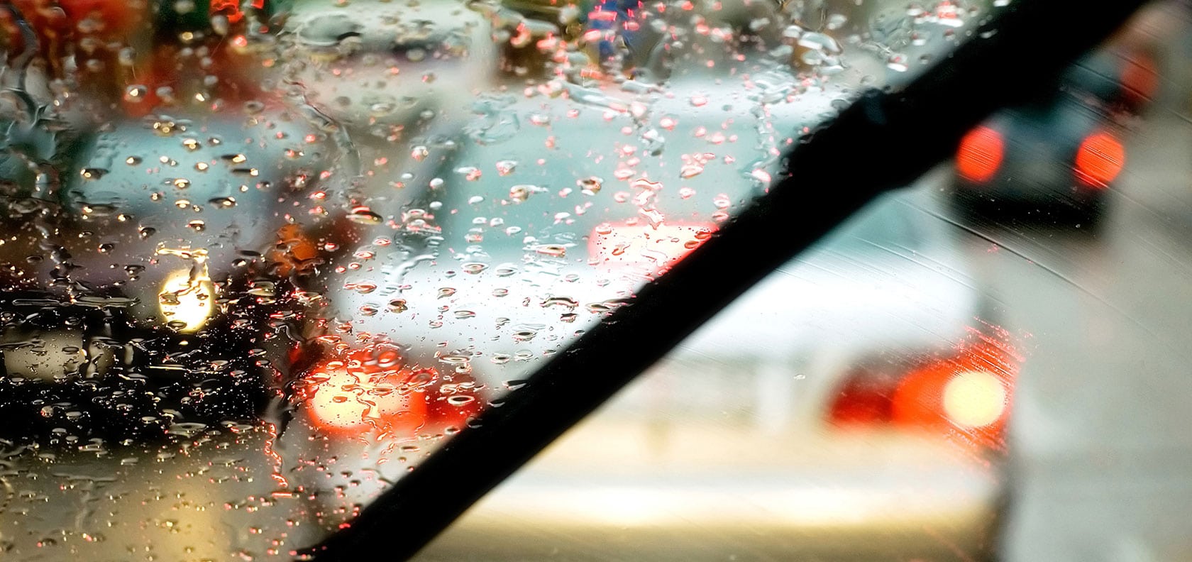 Windshield wipers wiping rain glass while it rains on the road.